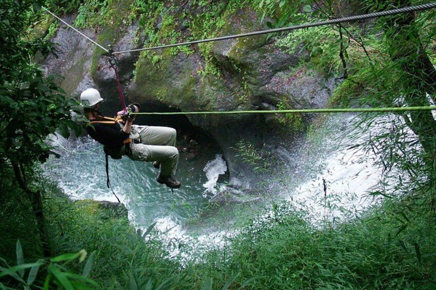 A person rappelling down a rocky cliff into a river surrounded by dense greenery. 5