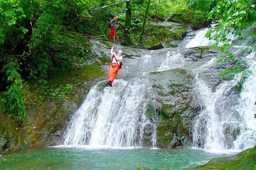 A person in red harness and white shirt performing a zip-lining activity over a waterfall. 3