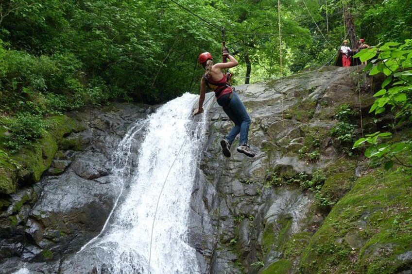 A person rappelling down a waterfall in a forested area. 2