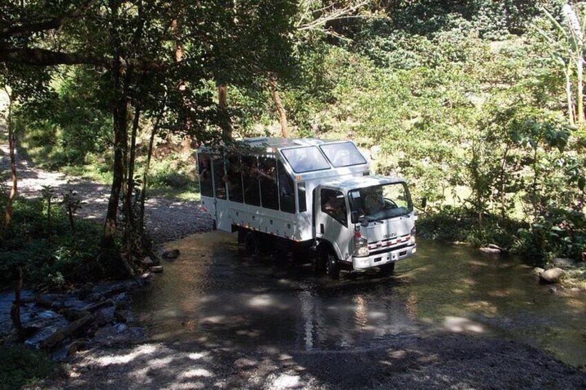 A truck crossing a shallow stream in a forested area. 5