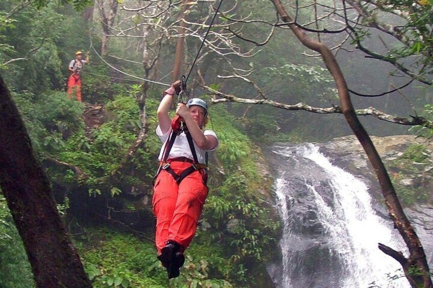 A person zip-lining through a forest with a waterfall in the background. 1