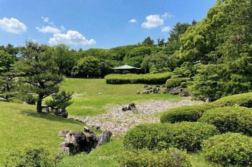 A serene Japanese garden with a large tree, neatly trimmed bushes, and a small pond. 3
