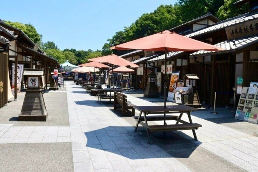 A traditional Japanese street with wooden buildings, red umbrellas, and stone lanterns. 2