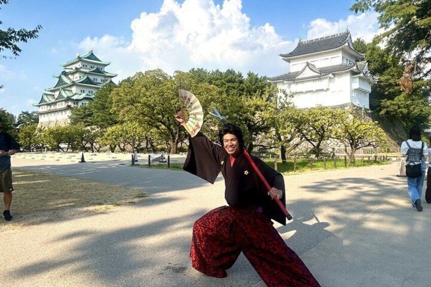 A person in traditional attire holding a fan, with a historic castle in the background. 1