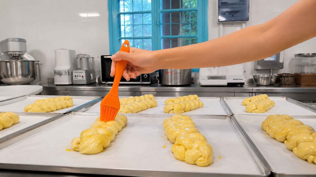 A person using an orange brush to apply a yellow substance to dough on a baking tray in a kitchen. 2