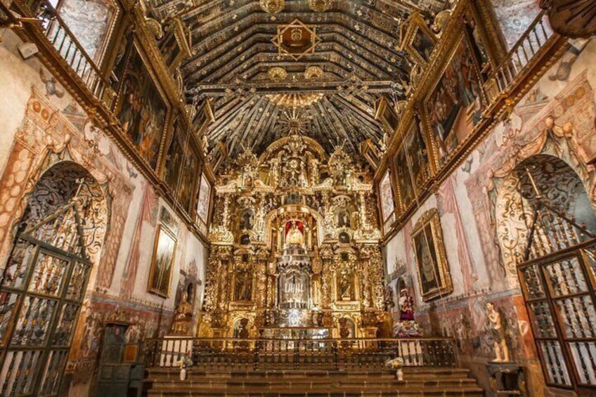 An ornate church interior with a high ceiling, detailed frescoes, and a central altar. 1