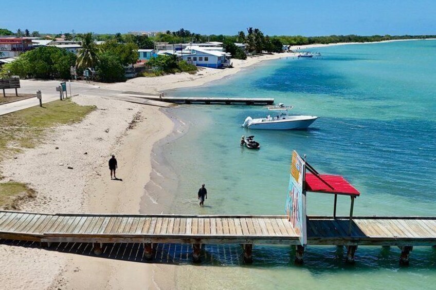 A beach with a wooden pier, clear turquoise water, and a few boats. 3