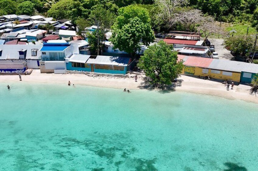 A coastal area with clear turquoise waters, a sandy beach, and several buildings with colorful roofs. 4