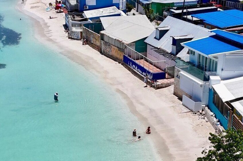 A beach with clear turquoise water, a sandy shore, and buildings with blue roofs. 5