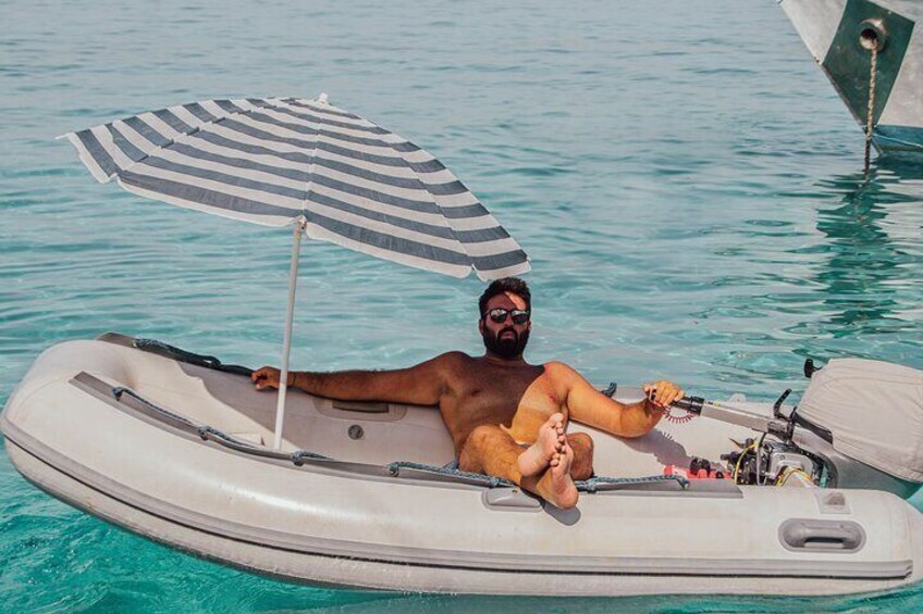 A person relaxing on a small inflatable boat in clear blue water, with a striped umbrella providing shade. 4