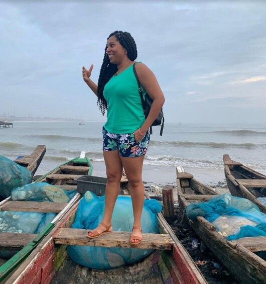 A person standing on a wooden boat at a beach with other boats and a pier in the background. 4