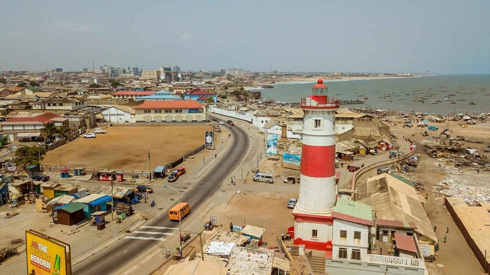 A coastal cityscape with a prominent red and white lighthouse, a busy road, and a beach with boats. 3