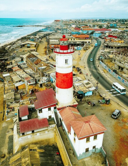 A coastal town with a prominent red and white lighthouse, narrow streets, and a beach in the background. 1