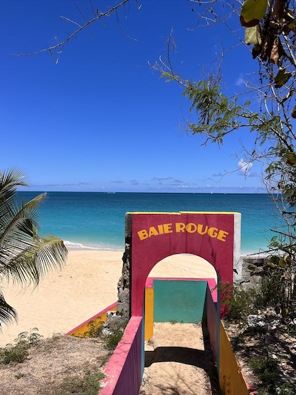 A beach entrance with a colorful archway labeled 'BAIE ROUGE' leading to a sandy beach and turquoise ocean. 5