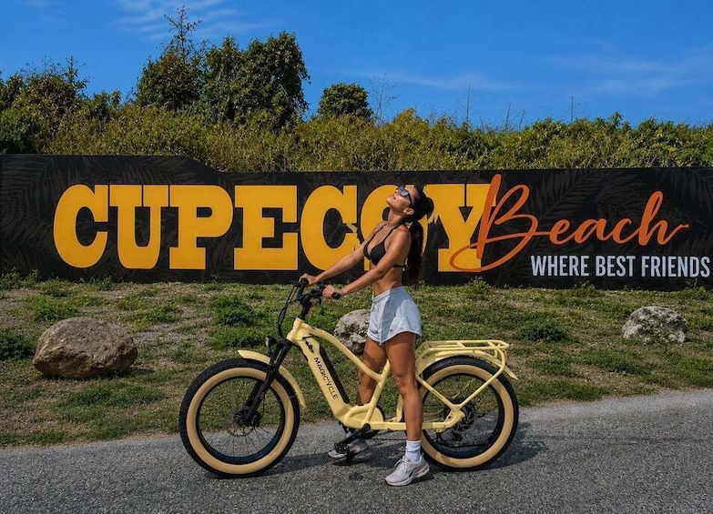 A person standing next to a yellow bicycle with a large sign in the background that reads 'CUPECOTY Beach.' 1