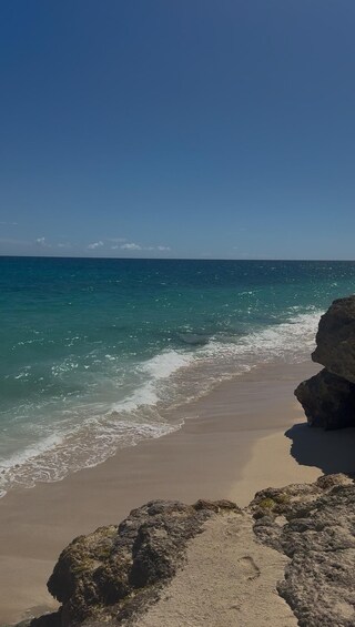 A beach with clear turquoise water, sandy shore, and rocky outcrops. 3