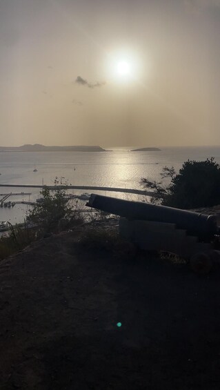 A sunset over a calm sea with boats, a distant landmass, and a large pipe in the foreground. 5
