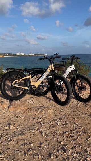 Two bicycles parked on a rocky shore with a coastal view in the background. 1