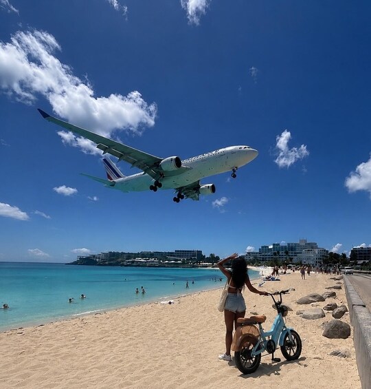 An airplane flying over a beach with people and a child on a tricycle. 2