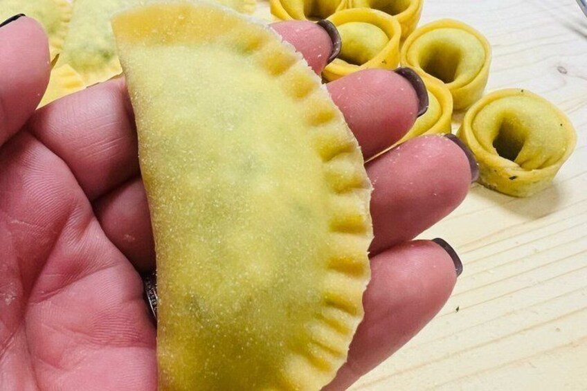 A hand holding a stuffed pastry with a crimped edge, surrounded by similar pastries on a wooden surface. 1