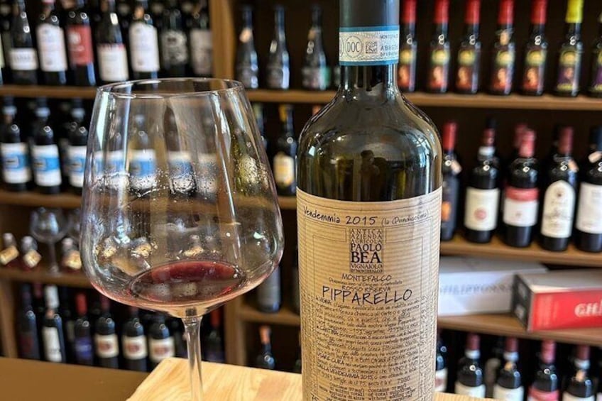 A wine bottle labeled 'Pipappello' and a wine glass on a table with a wine rack in the background. 4