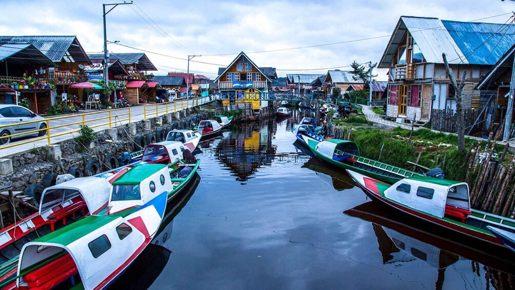 A canal with boats docked on both sides, surrounded by wooden houses with metal roofs. 3