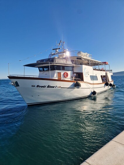A white boat named 'Sveti Sime I' docked at a pier with calm water and a clear blue sky. 5