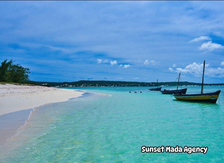 A beach with clear turquoise water, a sandy shore, and several boats anchored near the water. 4