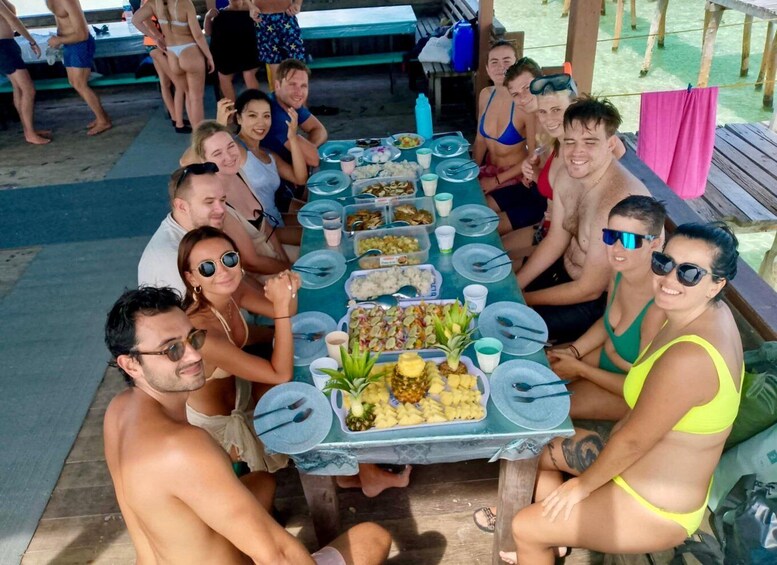 A group of people seated around a table with food and drinks, outdoors. 2