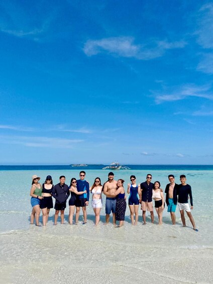 A group of people standing on a beach with the ocean and boats in the background. 5