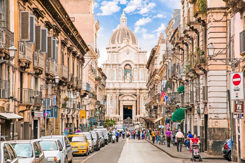 A bustling street with historic buildings, a prominent church with a dome, and a crowd of people. 2
