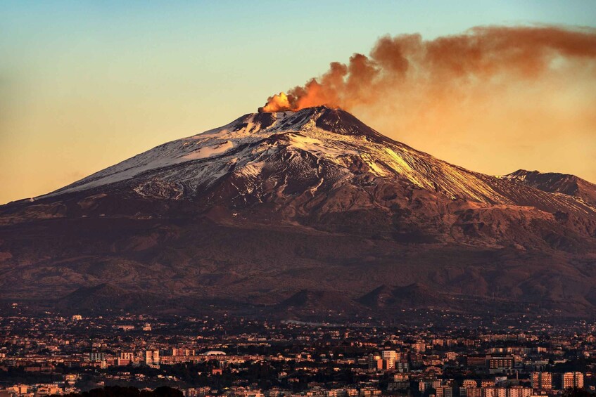 A snow-capped volcano erupting with smoke, a cityscape in the foreground, and a clear sky. 5