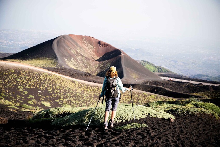 A hiker with a backpack and trekking poles walking on a volcanic landscape. 1