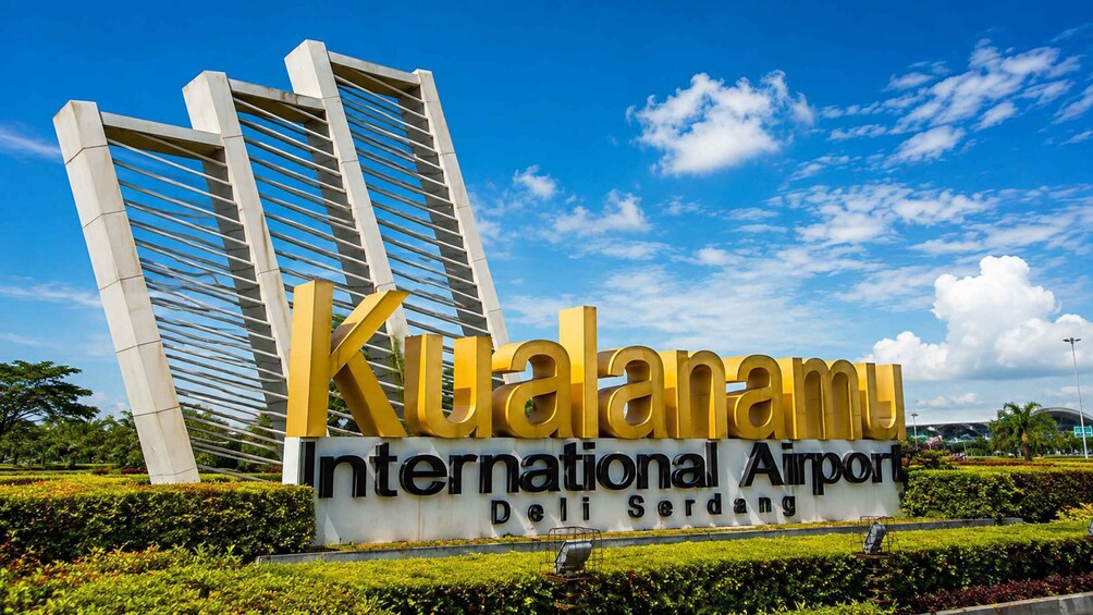 A sign for Kualanamu International Airport with a modern building in the background. 2