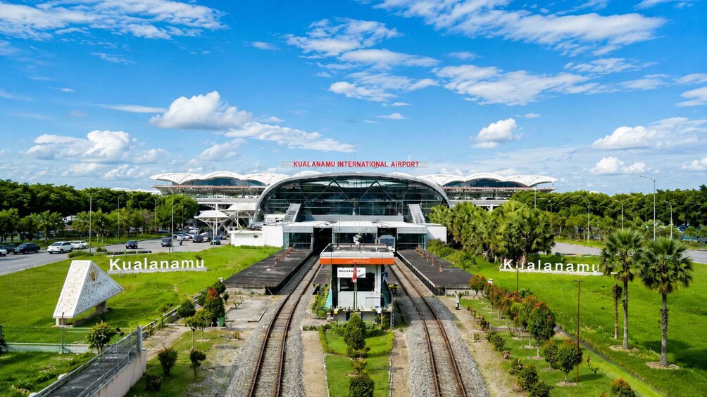 KUALANAMU INTERNATIONAL AIRPORT with a modern terminal structure, multiple tracks, and surrounding greenery. 3