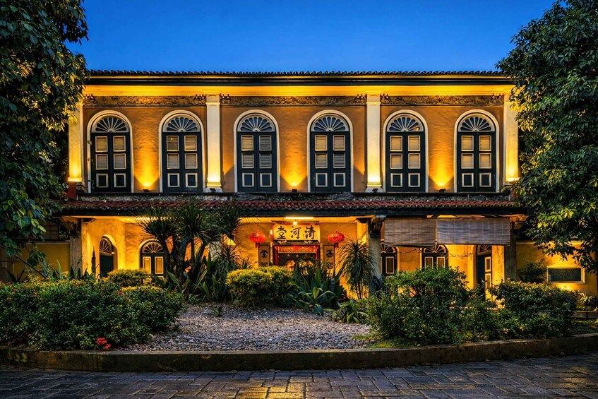 A traditional building with arched windows and a tiled roof, surrounded by lush greenery and a gravel pathway. 4