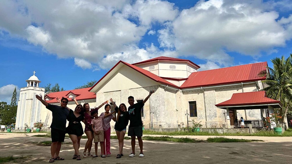 A group of people posing in front of a church with a red roof and a bell tower. 4