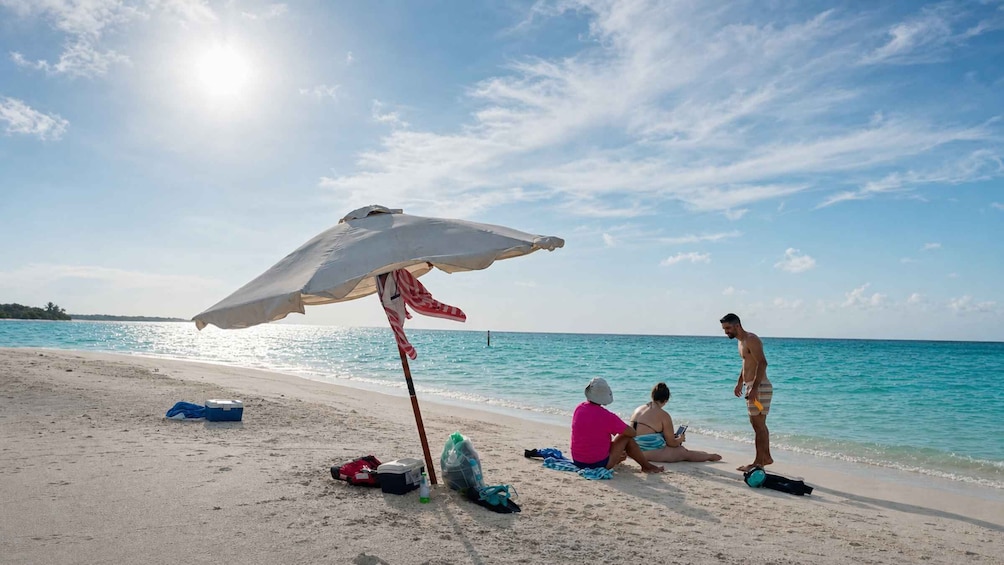 A beach with a white umbrella, people relaxing, and a clear blue sky. 3