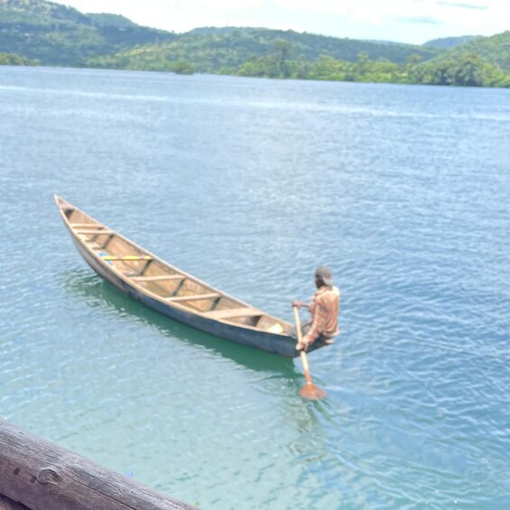A person rowing a wooden canoe on a calm lake with hills in the background. 1