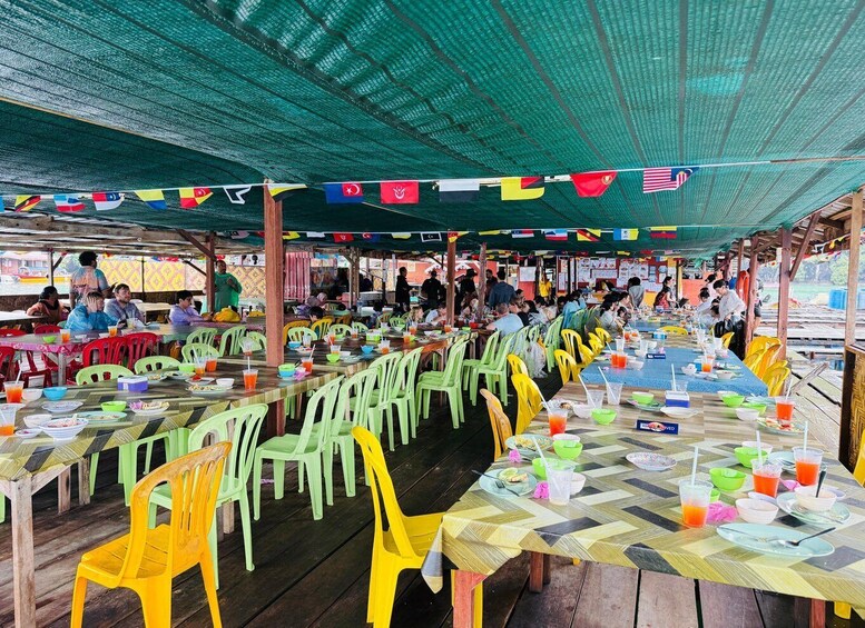A crowded outdoor dining area with colorful plastic chairs and tables, under a green canopy. 3