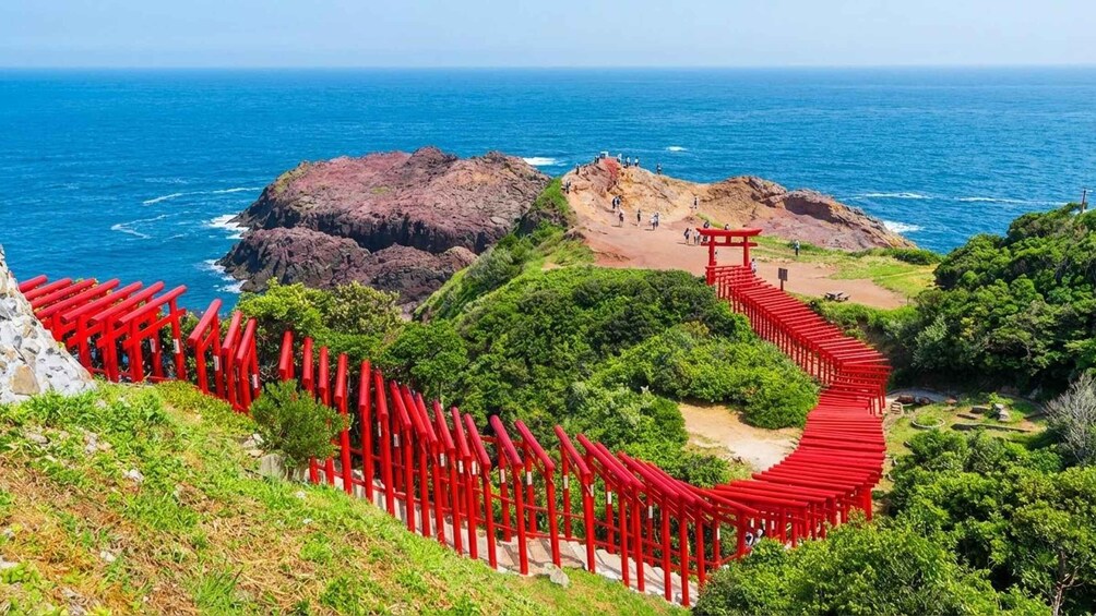 A red wooden walkway leading to a traditional Japanese torii gate, surrounded by lush greenery and overlooking the ocean. 3