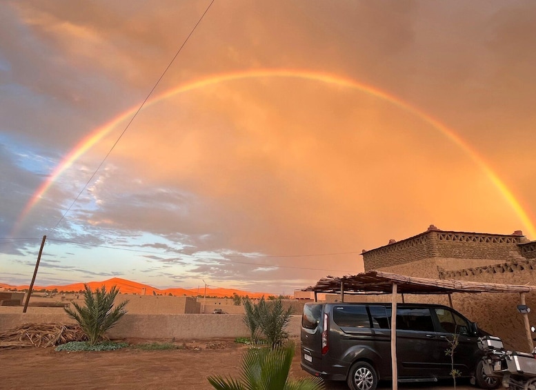 A rainbow over a desert landscape with a building and a parked car. 5