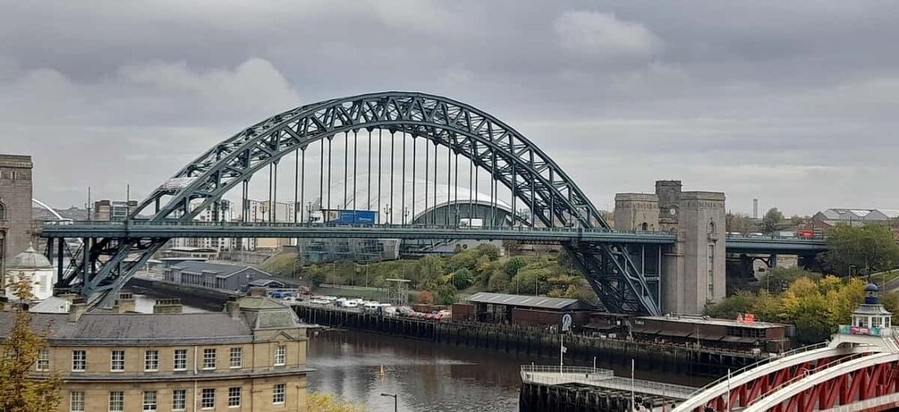 A large steel bridge spanning a river, with buildings and a dome structure in the background. 1