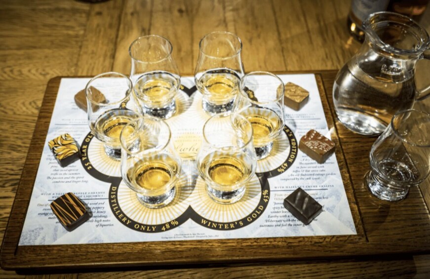 A tray with shot glasses filled with a golden liquid, arranged on a menu with text and images of food. 2