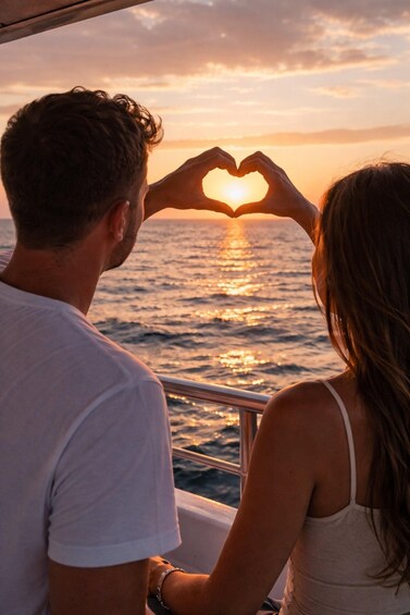 A couple making a heart shape with their hands, facing the sunset over the ocean. 5