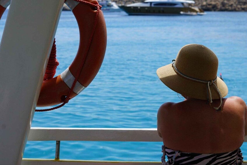 A person wearing a straw hat and striped swimwear, looking out at a body of water with a boat in the distance. 5