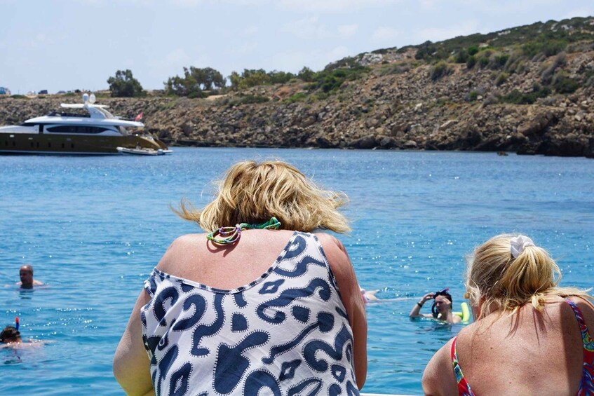 A group of people swimming in a body of water with a yacht in the background. 4