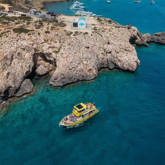A rocky coastline with clear blue waters, a yellow boat with passengers, and several yachts docked nearby. 1