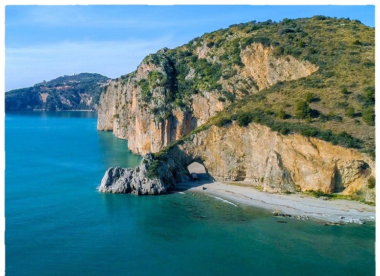 A coastal landscape with a rocky cliff, a clear blue sea, and a small beach. 2