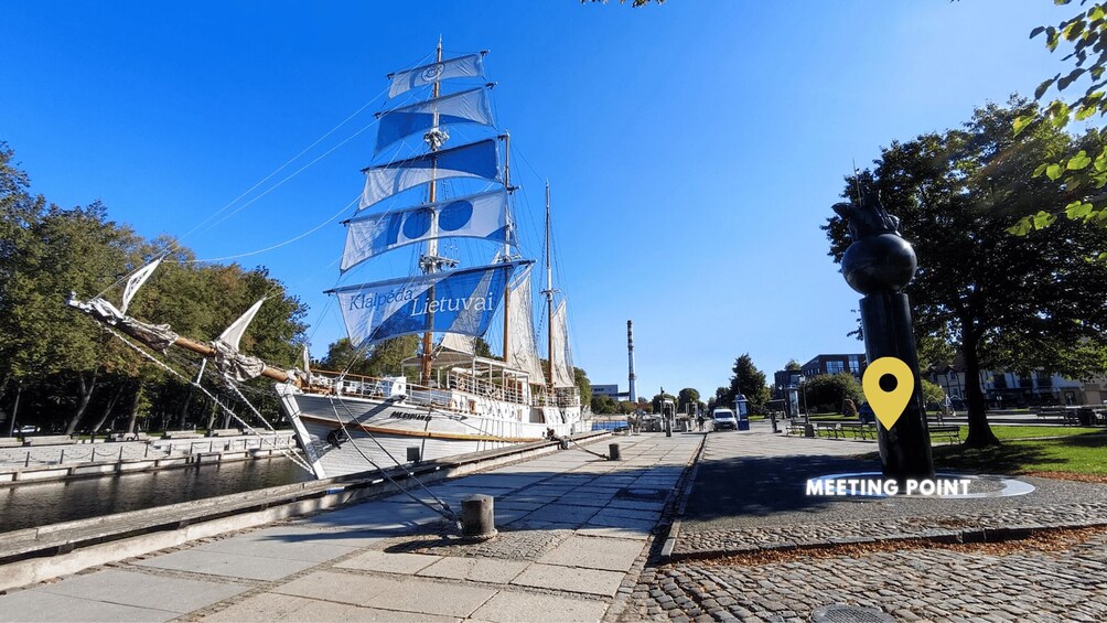 A tall sailing ship docked at a waterfront, a statue, and a 'Meeting Point' sign. 5